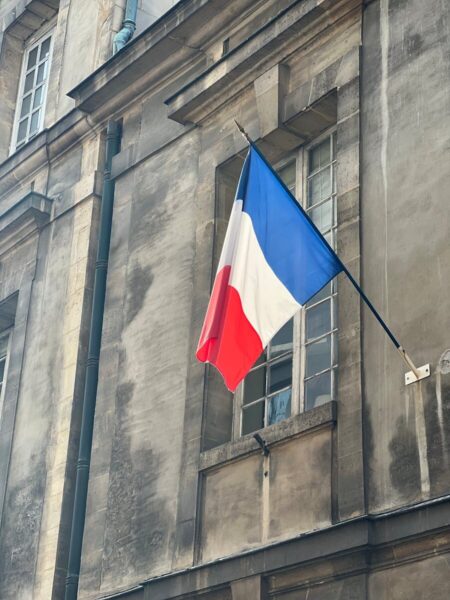 Vertical shot of the French flag on a classic building facade; symbolizes France's heritage.