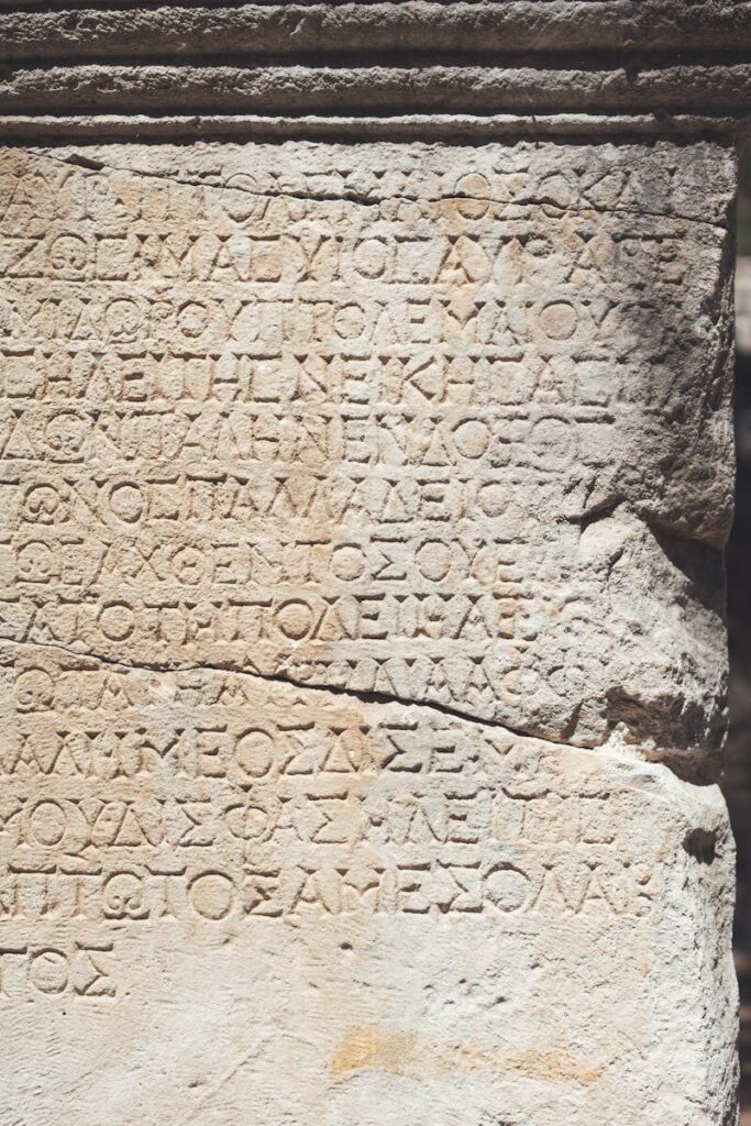 Close-up of ancient Greek stone inscription with detailed carved text under sunlight.