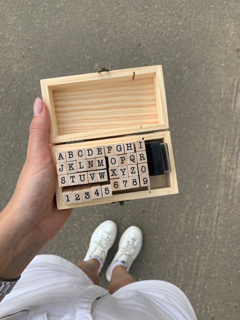 Overhead view of a wooden box containing alphabet rubber stamps being held by a person.