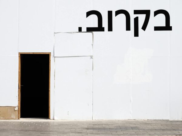 Simple white wall with a black door and Hebrew text, offering urban minimalism.
