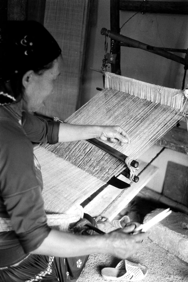 Black and white photo of a woman weaving on a loom, highlighting traditional craftsmanship.