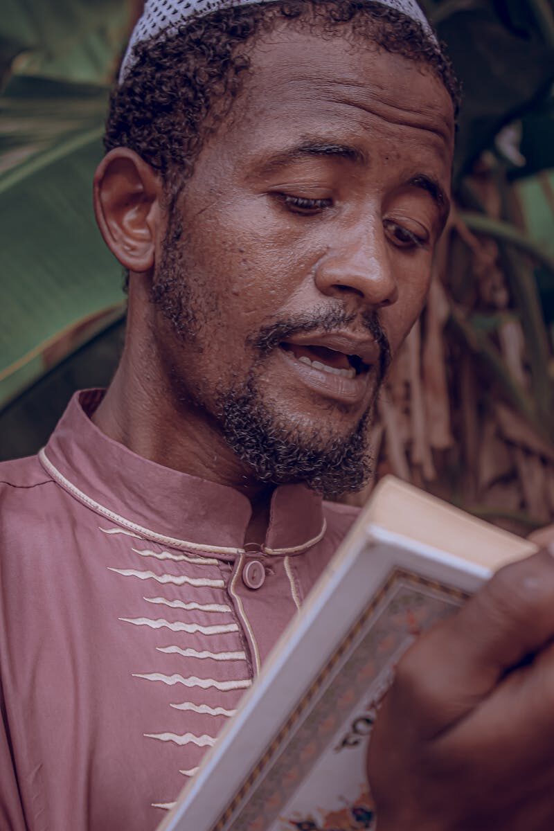 Man in traditional clothing reading a book outdoors, showcasing cultural expression.