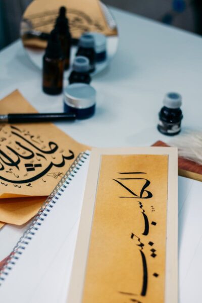 Close-up of Arabic calligraphy art with ink bottles and brush on a desk.