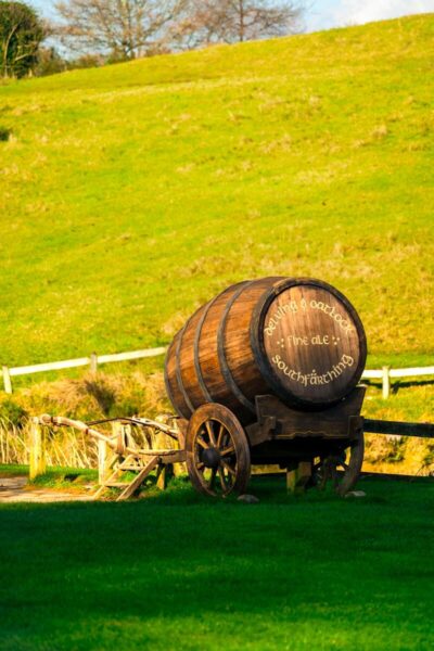 Wooden ale barrel cart in lush Hobbiton, captured under sunny skies in Matamata, New Zealand.