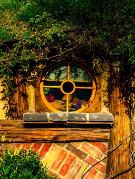 A picturesque wooden window from a hobbit hole in Matamata, New Zealand, surrounded by greenery.