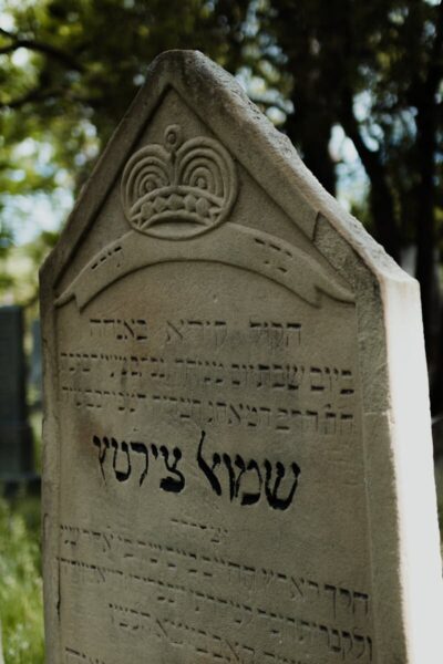 Close-up of a historical Jewish gravestone with Hebrew inscriptions in an outdoor cemetery.
