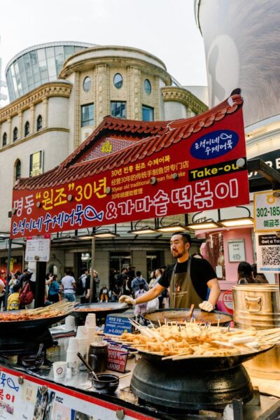 Bustling street food scene in Myeongdong, Seoul featuring a vendor selling traditional Korean dishes.