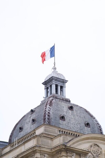 French flag flying on a historical building dome in Paris, showcasing classic architecture.