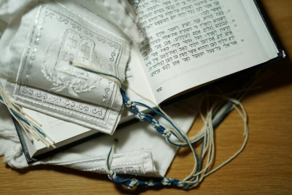 Open Hebrew Bible with a Tallit and Siddur on a wooden table, symbolizing Jewish tradition and religion.
