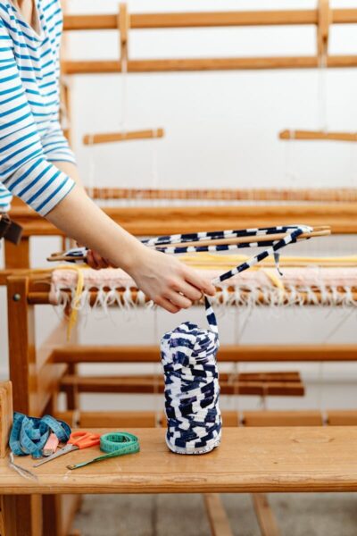 A person weaving fabric on a wooden loom, showcasing yarns and tools.