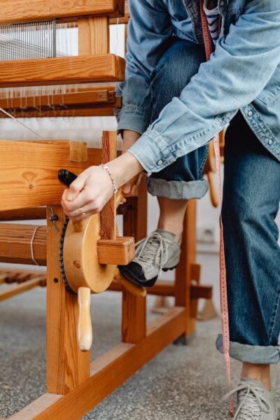 Detailed shot of a woman using a wooden loom in a textile workshop, showcasing craftsmanship.