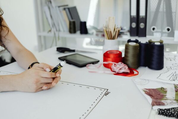 Fashion designer's workspace with ribbons, sketches, and tools on a white desk.